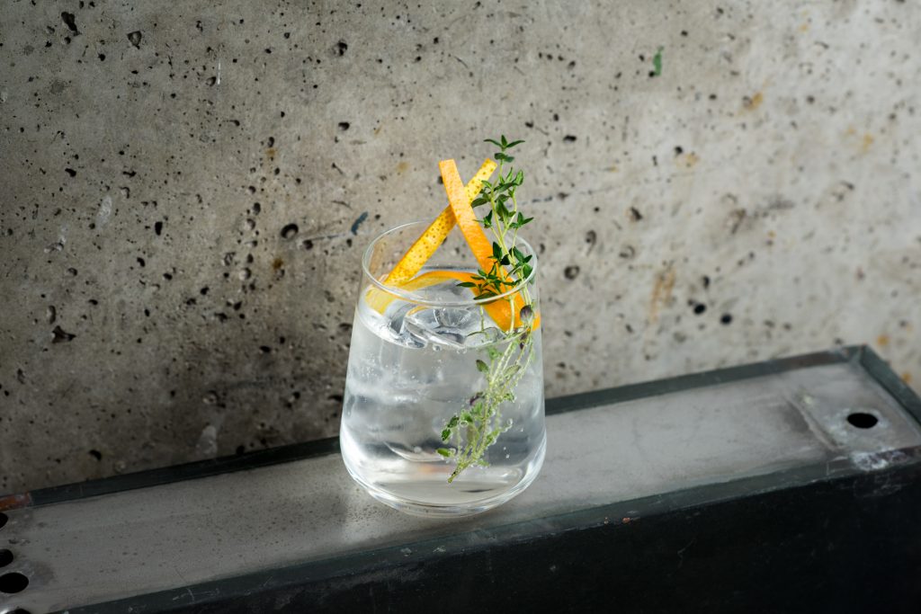 Raikkaannäköinen G&T eli Gin & Tonic cocktail betoniseinää vasten kuvattuna.