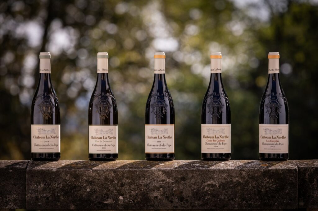 Château La Nerthen viinipulloja kivisen aidan päällä auringonvalossa.