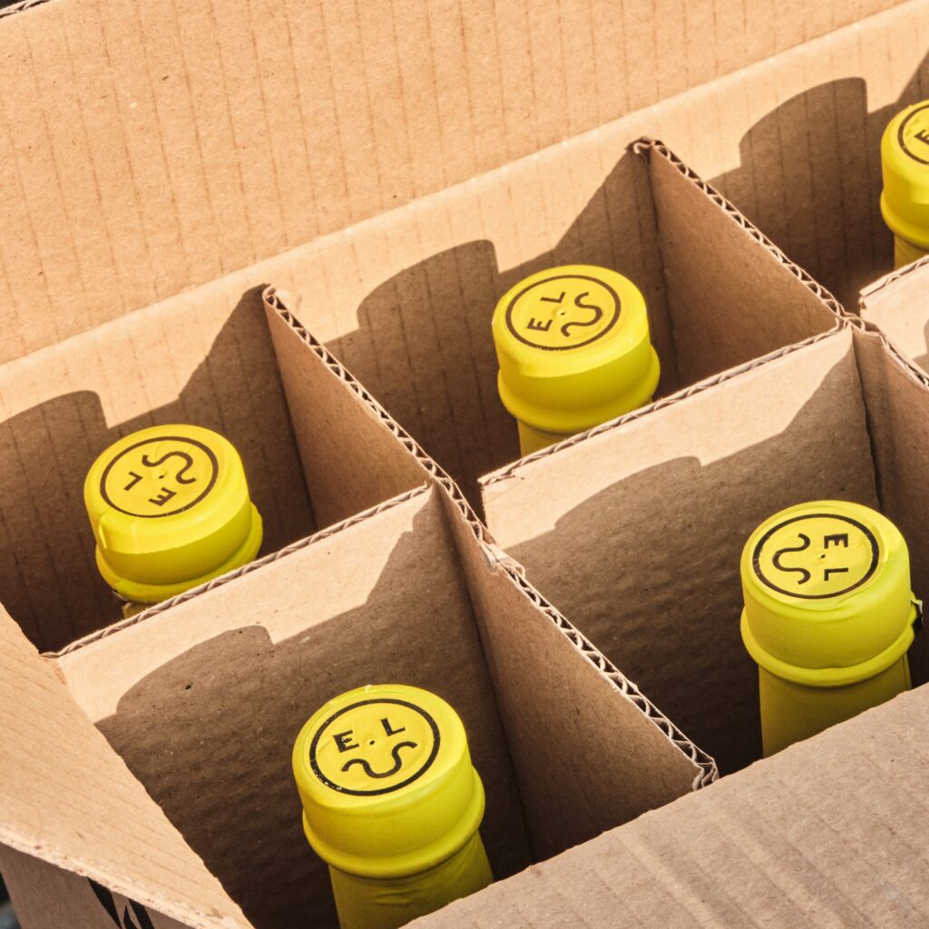 Keltaisia East London Liquor Companyn korkkeja pilkistämässä pahvisesta pullolaatikosta.