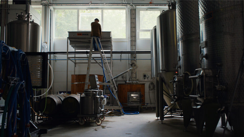 Mies kiivenneenä korkeille tikkaille korkean altaan äärelle, joka on avatun ikkunan alla. Ympärillä näkyy suuria terästankkeja.