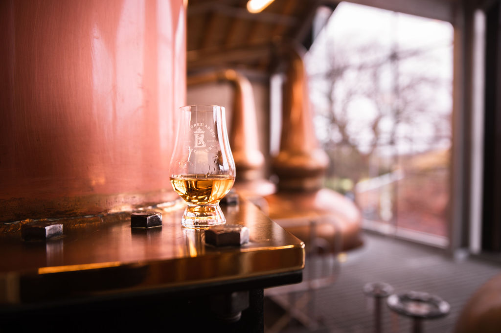 Viskilasi edustalla, taustalla tislaamolaitteita.