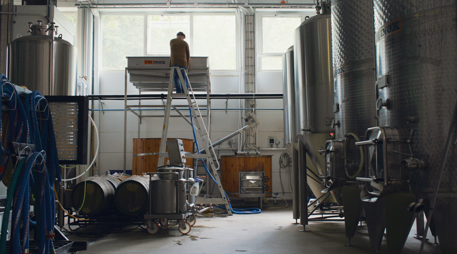 Panimoympäristössä terästankkeja, ja korkea laakea astia eli koelschip ikkunan äärellä, jonka äärelle on kiivennyt mies korkeilla tikkailla.