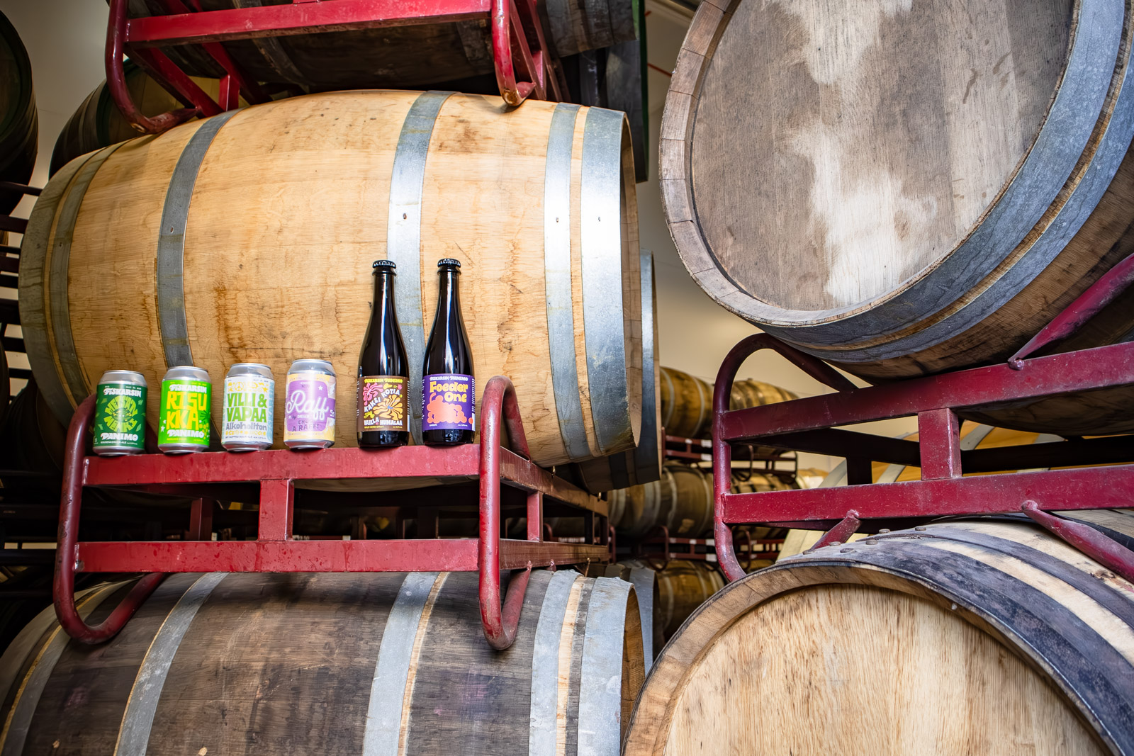 Fiskarsin Panimon oluita kuvattuna tammitynnyreiden edessä. Taustalla näkyy useita rivejä tynnyreitä.